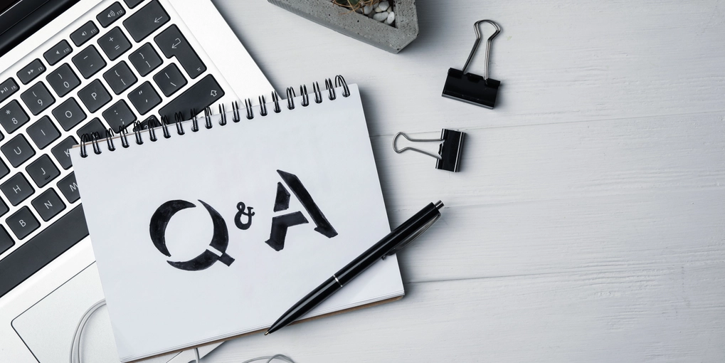 A laptop on a desk with a notebook on top with Q&A written in it