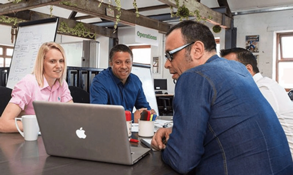 A group of three people discussing something they are looking at on the laptop in an office