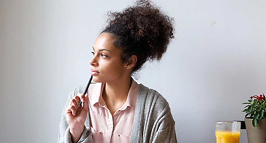 Woman holding pen to lip and staring to the left