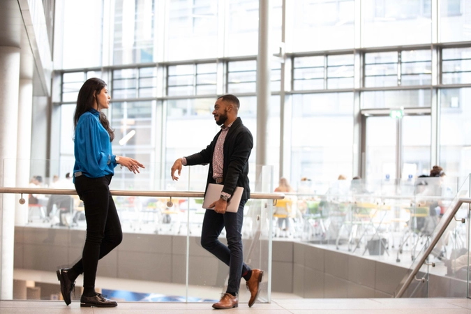 Two MBA students standing against a glass railing in TBS lobby