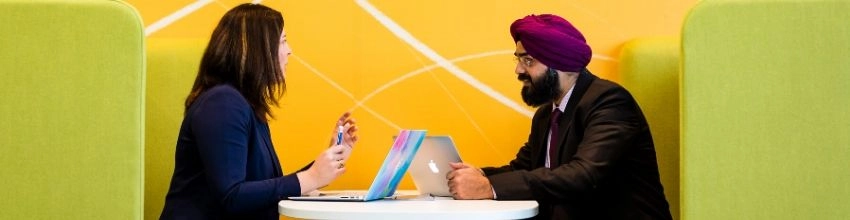 Two MBA Students sitting in a booth with laptops in conversation