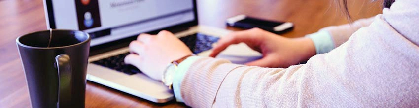 Man on laptop typing with a cup to the left