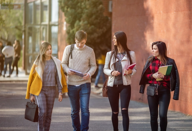 Four students walking together outside holding folders