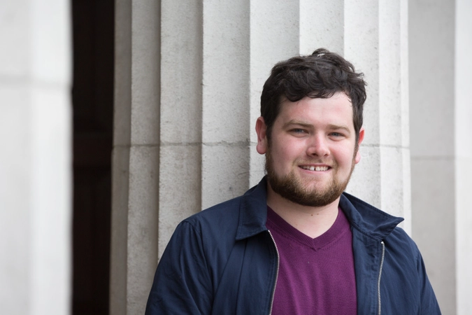 A student standing in front of a granite pillar wearing a navy jacket and purple tshirt