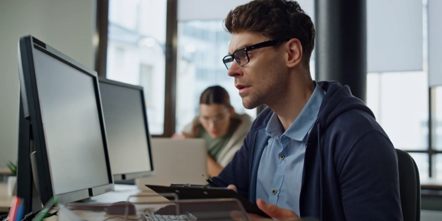 A person in a blue shirt and glasses sitting at a desk with a computer