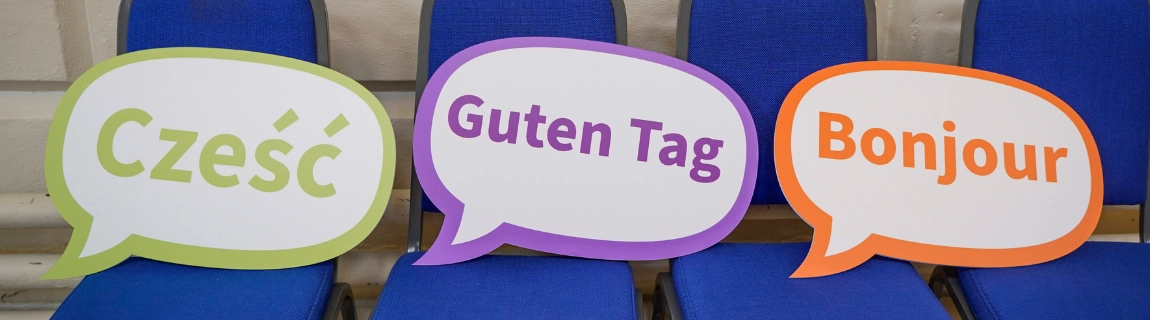 Speech bubble signs displaying a greeting in the Polish, German and French languages.