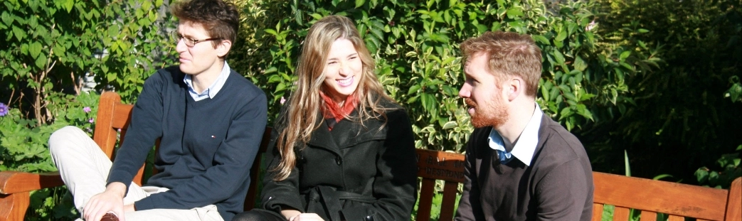 Three young postgraduates chatting while sitting on a bench in Trinity College Dublin