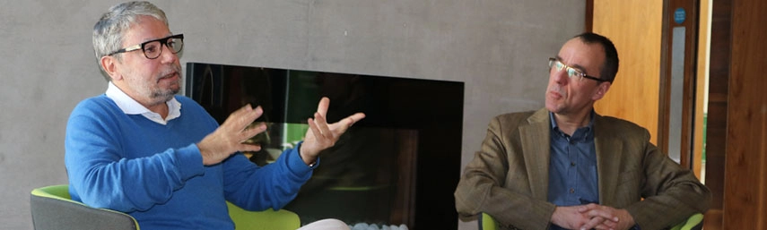 One man speaking to another at a circular table at the Long Room Hub