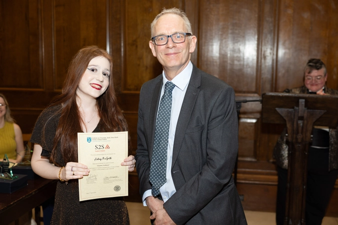 student smiling holding cert paper standing beside man in suit with tie