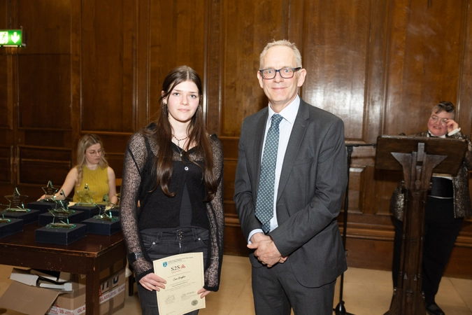 student in black dress holding cert paper beside man in suit
