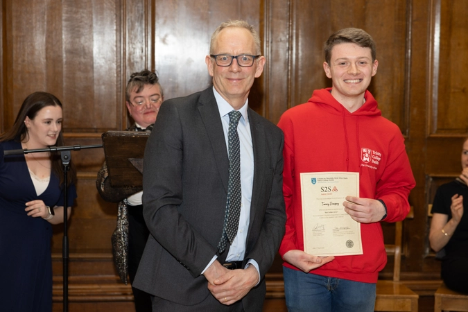 man in suit with tie smiling beside volunteer in red hoodie holding certificate