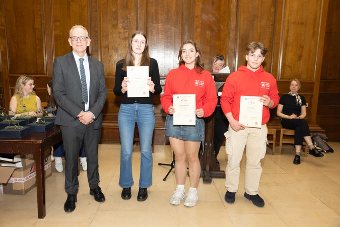 man in suit standing beside three volunteers. all volunteers are holding certificates. one volunteer is wearing a black top and the other two volunteers are wearing red hoodies