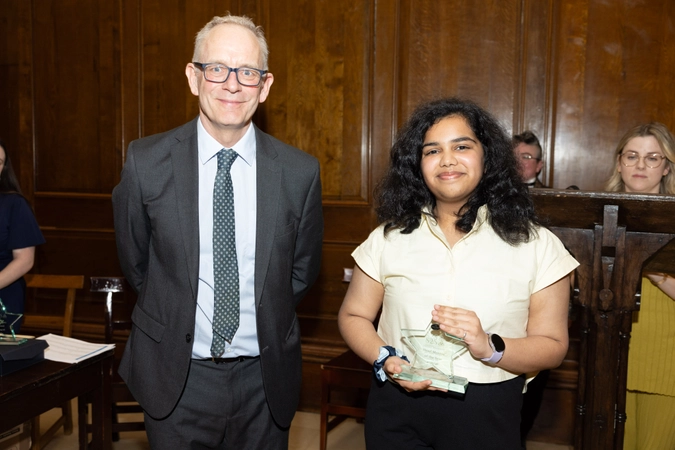 man wearing suit with glasses and tie standing beside volunteer in cream shirt holding star shaped trophy