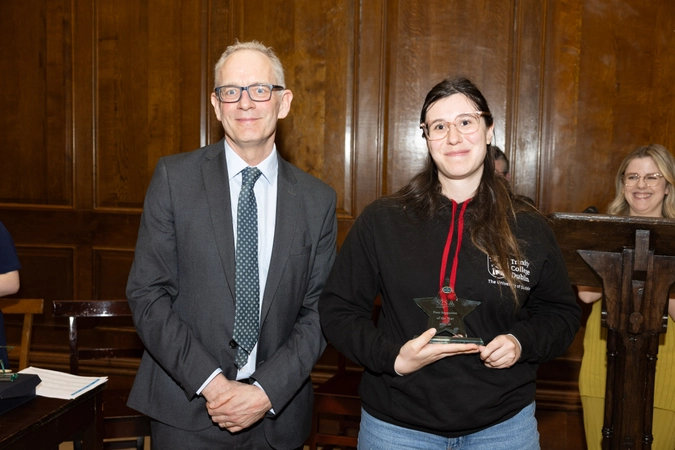 man in suit wearing glasses and tie smiling standing beside volunteer in black hoodie holding star shaped crystal trophy