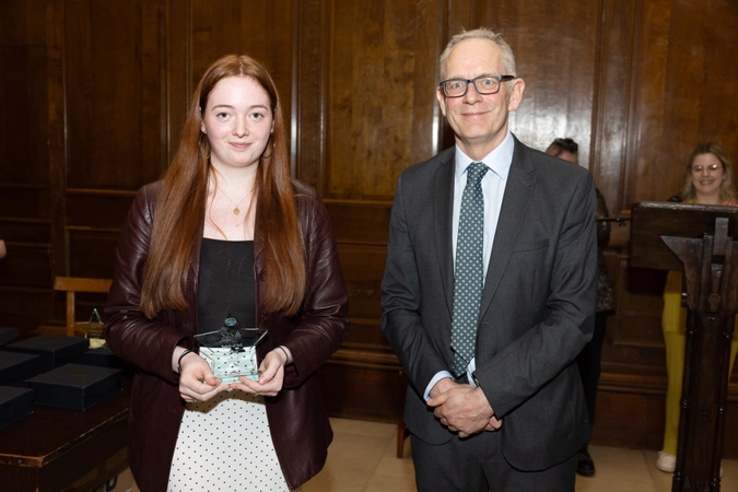 Women with red ginger hair holding crystal star trophy standing beside man in suit with tie and glasses