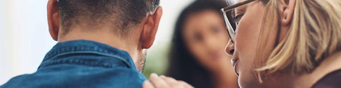 Woman placing hand on mans shoulder facing a blurred out woman