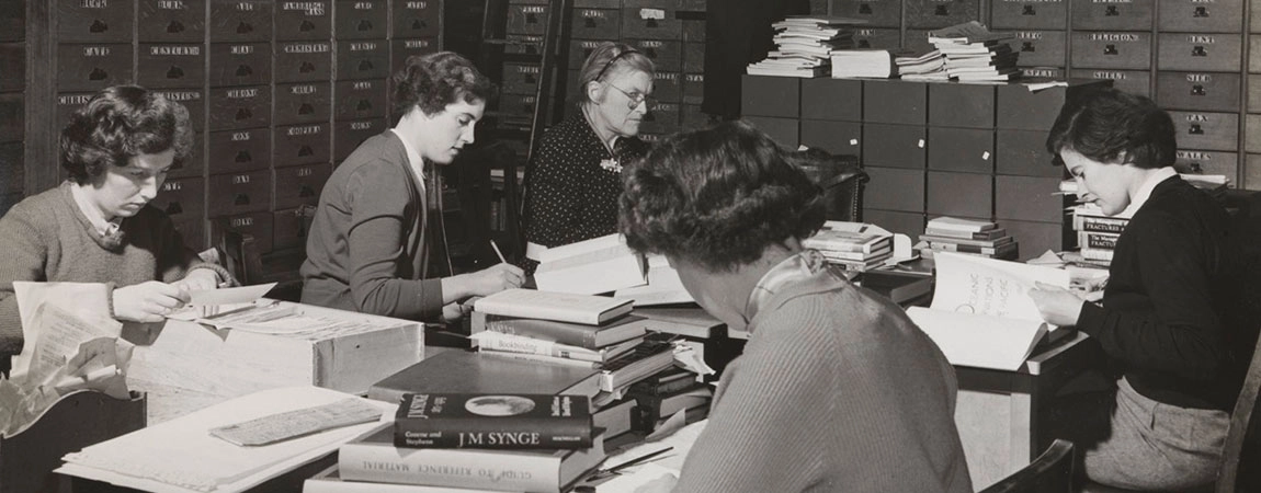 black and white oldtime image of women editors surrounded by books and filing cabinets