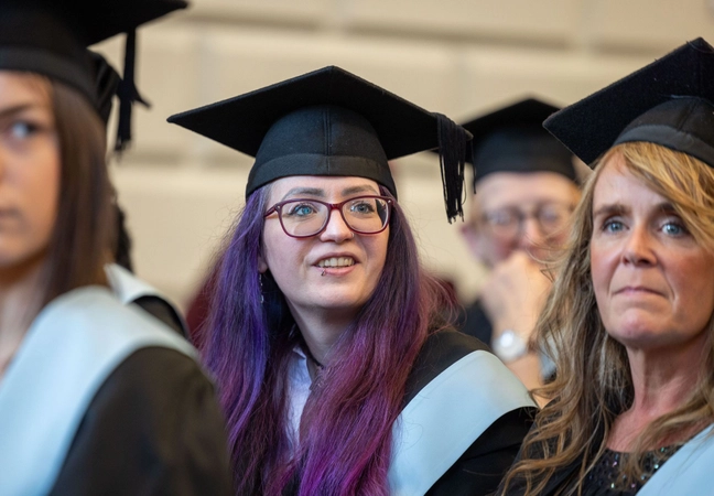Student in a graduation gown sitting down looking into the distance