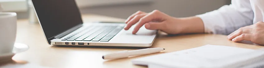 hands typing on laptop with a notebook and paper in the foreground