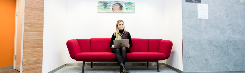 Woman student sitting on a red couch looking up from her laptop