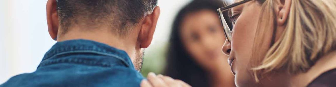 Woman placing hand on mans shoulder facing a blurred out woman