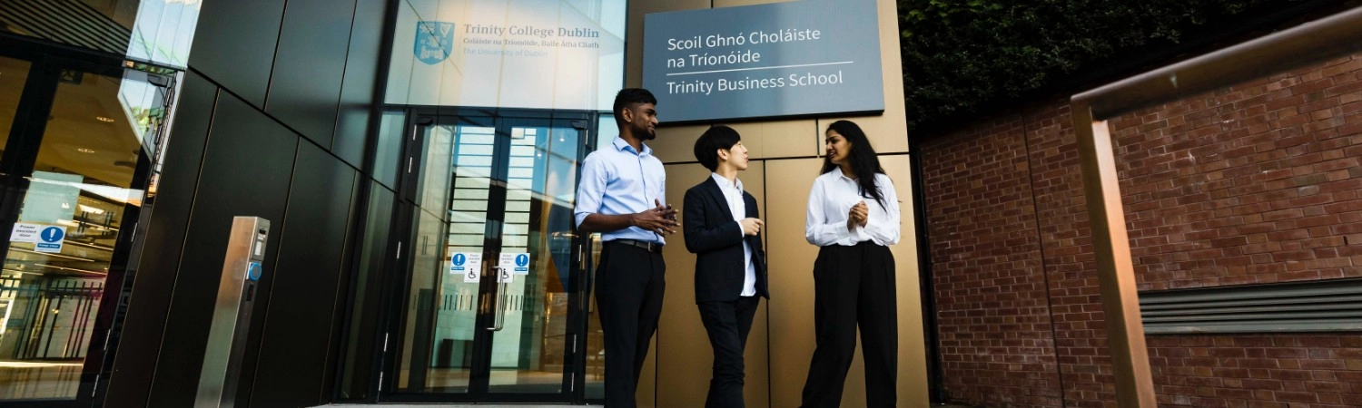 An image showing three people in front of the entrance to the Trinity Business School