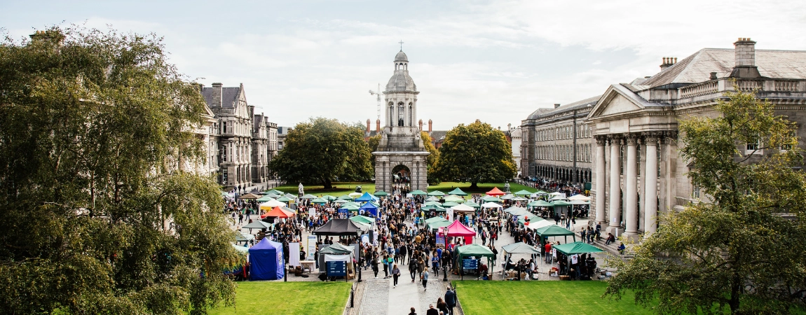 An image of all the stands set up on Front Square during Freshers' Week. There are people walking in to Front Square from Front Arch, past the green areas in Front Square