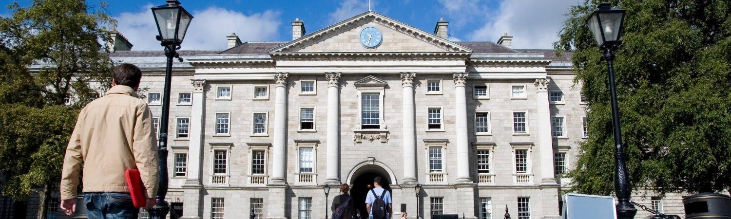 An image of a person walking towards the front building of Trinity College Dublin