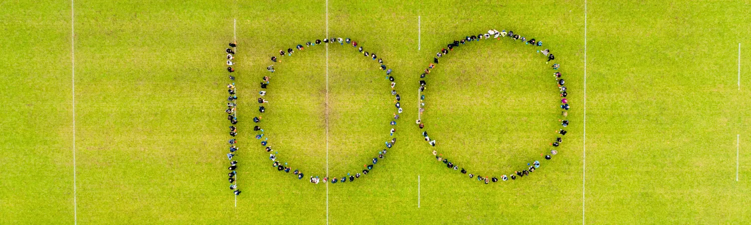 A group of people on the rugby pitch forming a shape of 100