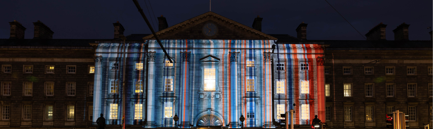 An image of Trinity's Front Gate with a projection of Dublin's Climate Stripes, designed by Professor Ed Hawkins