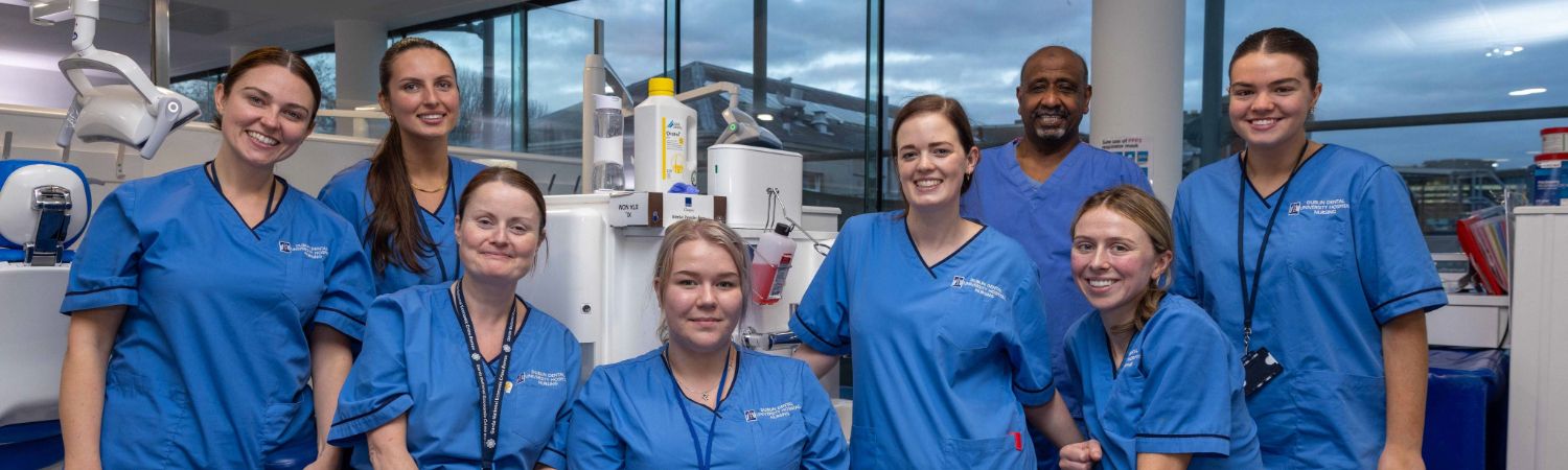 Eight dental students posing in front of a dental chair in The Dental Hospital