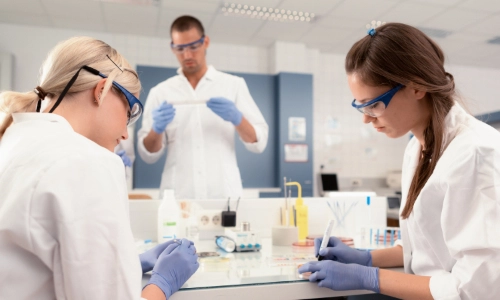 Three students wearing lab coats and blue gloves carrying out experiments