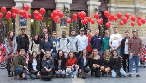 A photo of students standing outside a building in holding red balloons