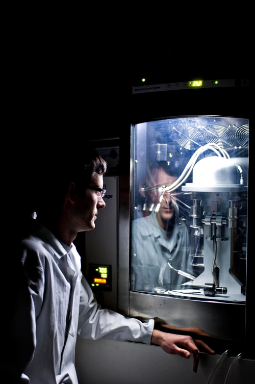 A student in a lab looking at a microscope inside a sealed cabinet