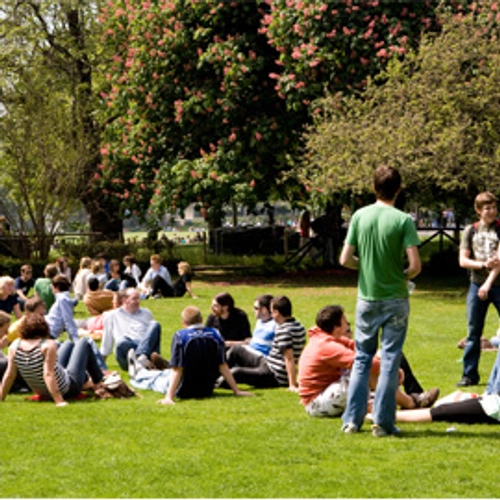 A group of people sitting on the cricket pitch outside the Pavilion Bar, Trinity College Dublin