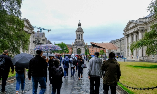 People holding unbrellas walking in to the Front Square of Trinity College Dublin