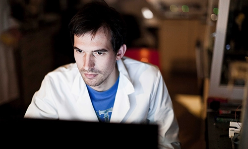 Researcher in white lab coat looking at screen