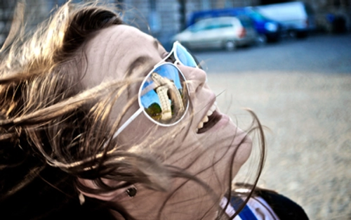 Trinity Student laughing with sunglasses that reflect the Trinity Campanile