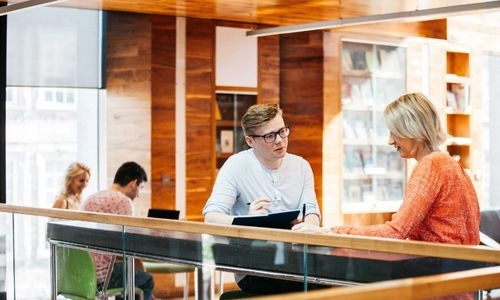 Two people speaking in the Long Room Hub meeting space.