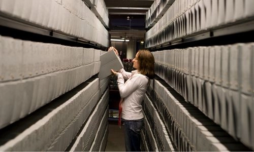 A person picking out a file from shelves in an archive room.