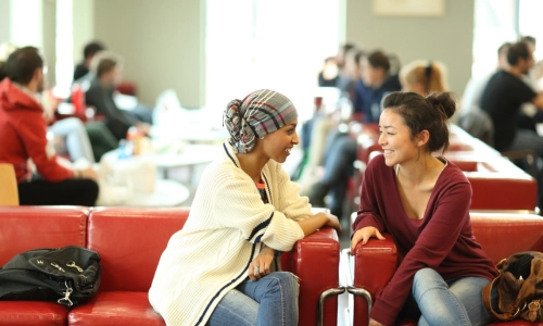 Two students seated on couches talking.