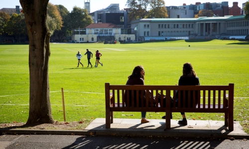 Two people sitting on a bench in front of Trinity College Park.