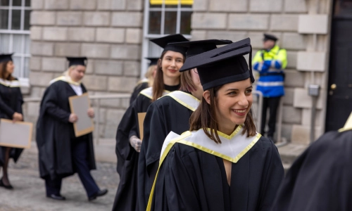Graduating students smiling while holding their diplomas.