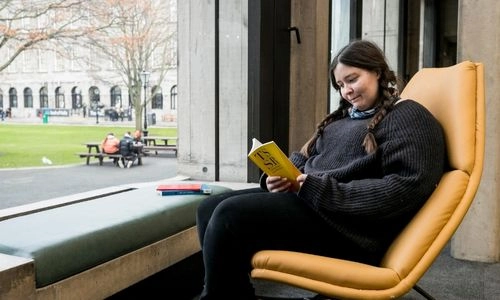 A student sitting reading a book in the Eavan Boland Library.