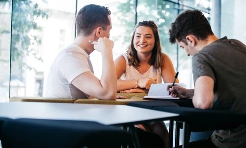 Three students seated together, one student takes notes.