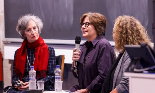 Three women at top of room, one speaking into mic
