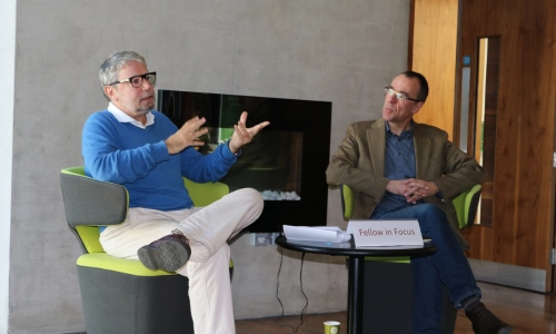 One man speaking to another at a circular table at the Long Room Hub