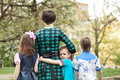 Three children standing beside an adult. One of the children is looking at the camera hugging the adult