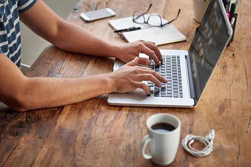 student typing on laptop with coffee on table