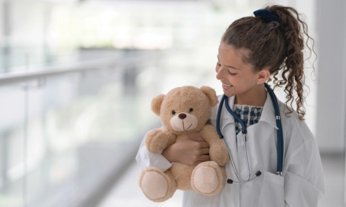 Child in medical coat holds teddy bear